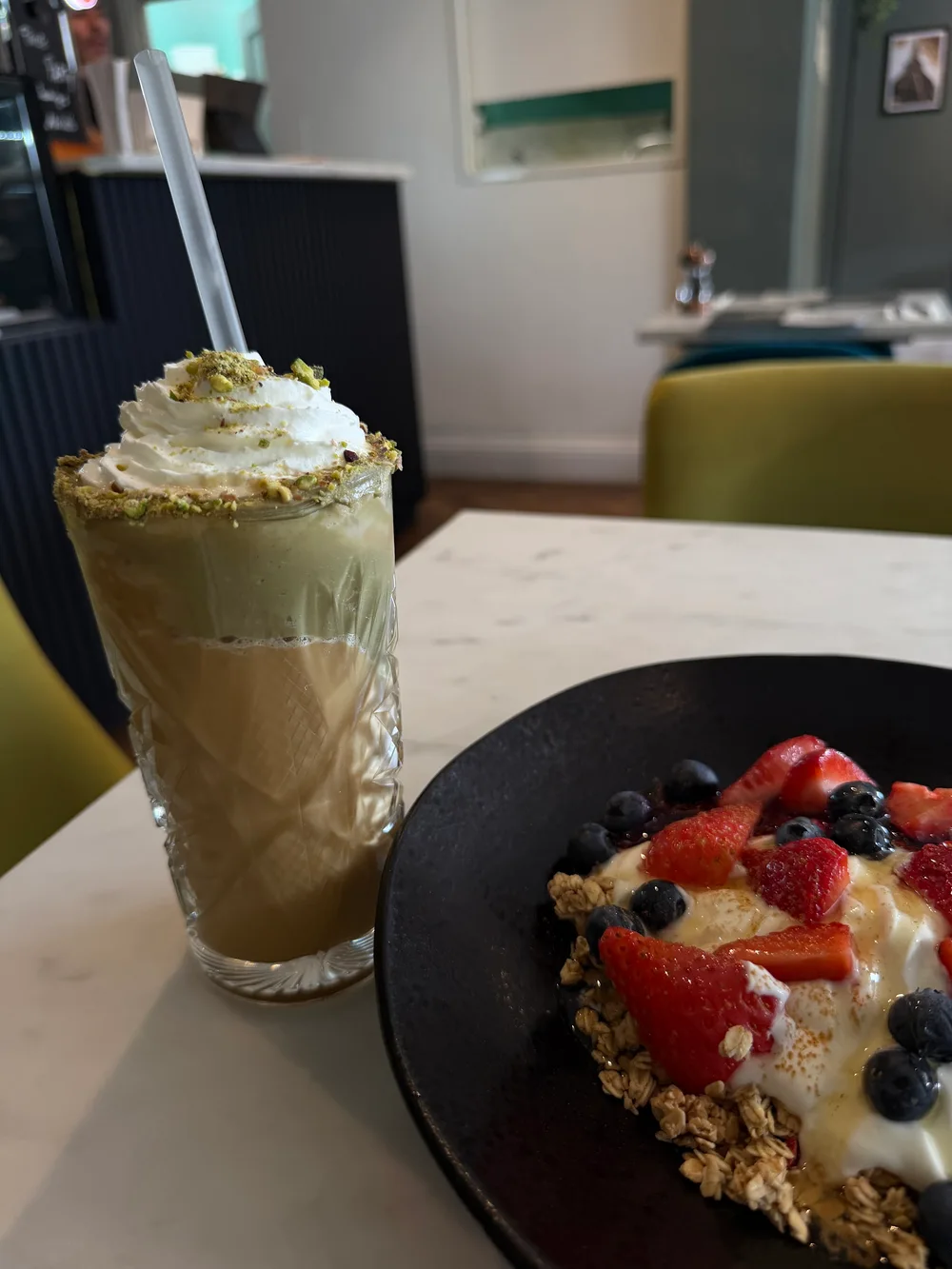 A breakfast bowl and iced drink beside the cafe's sage seating